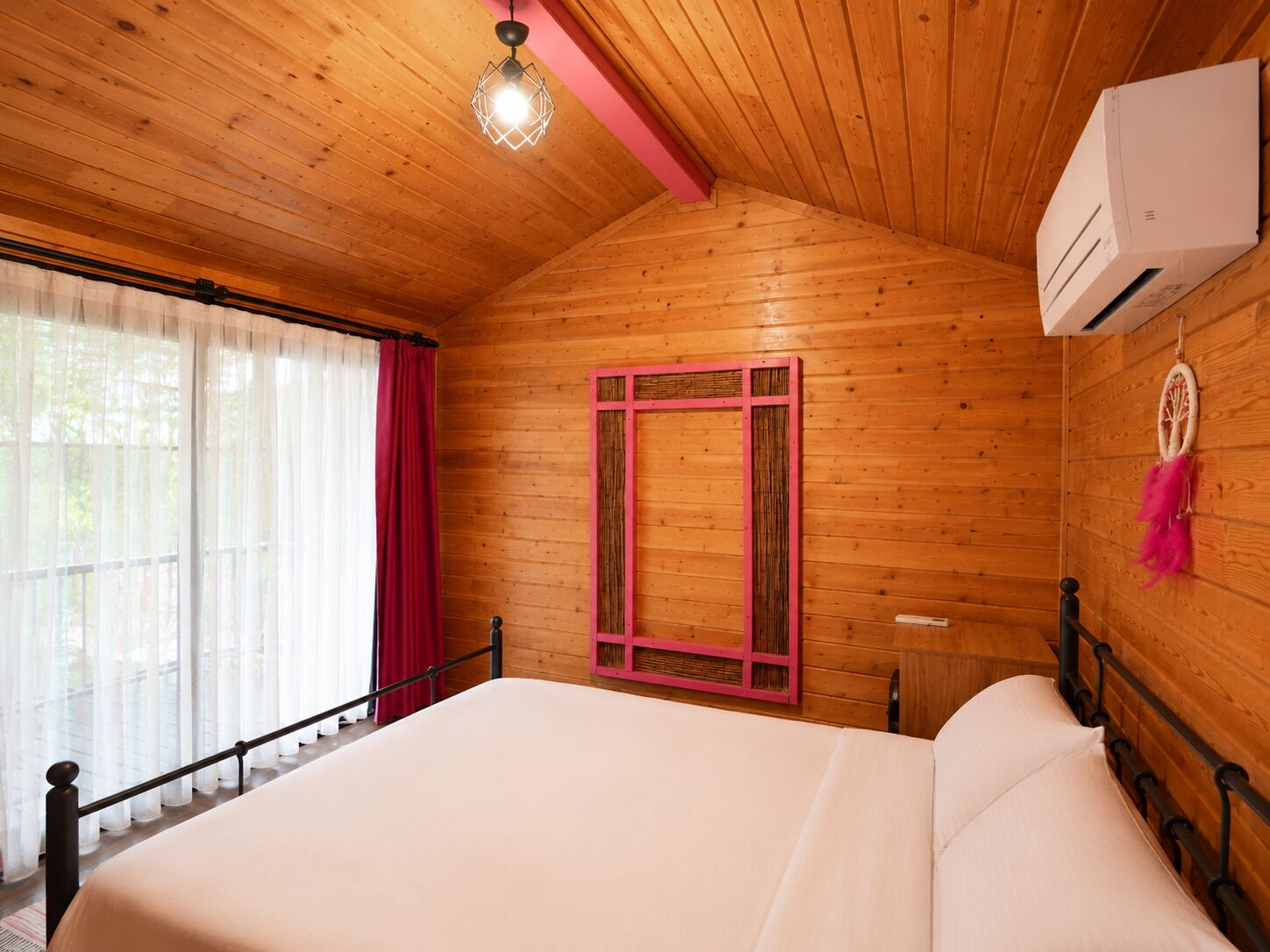 A wooden room with a bed, a window with curtains, a wall-mounted air conditioner, and a dreamcatcher.