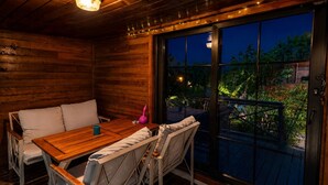 Een houten terras met een tafel en stoelen, een schuifdeur en uitzicht op groen.
