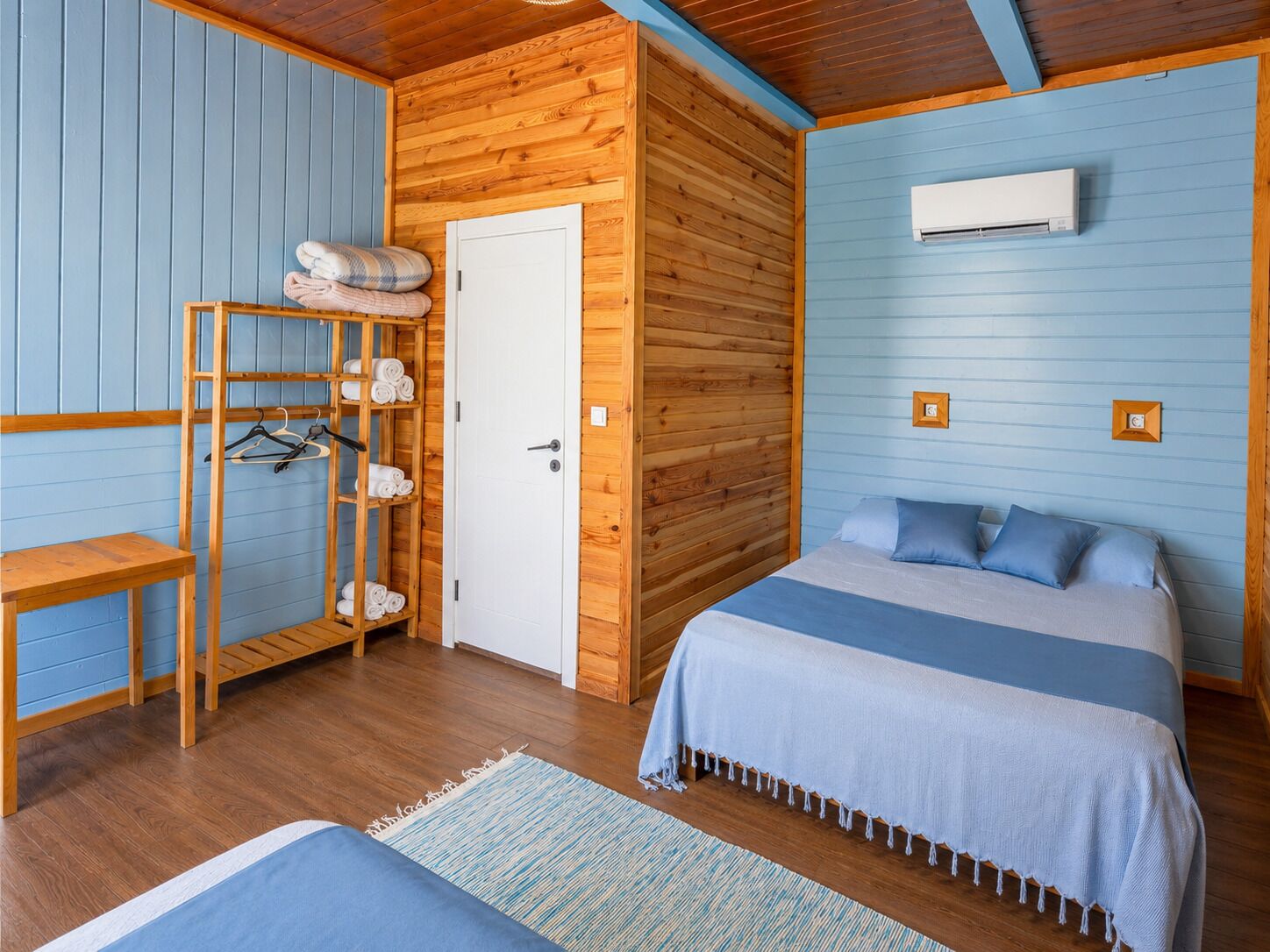 A room with a wooden bunk bed, a wooden wardrobe, a small table, and an air conditioning unit.