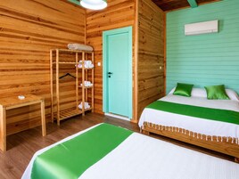 Una habitación de madera con una cama, una puerta verde, un perchero y una mesita.