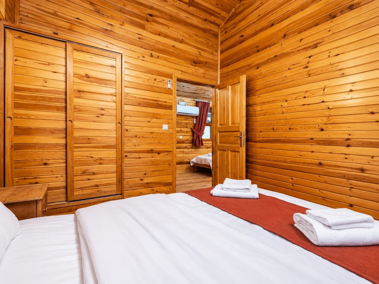 A wooden room with a bed, a wooden wardrobe, and a door leading to another room.