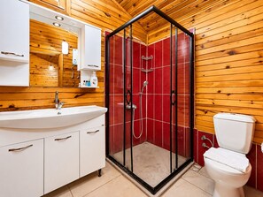 Casa de banho com painéis de madeira, cabine de chuveiro em vidro, lavatório branco e sanita.