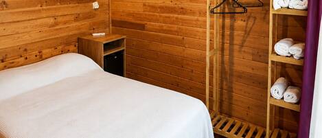 Una habitación de madera con una cama, un estante con toallas y una lámpara colgante.
