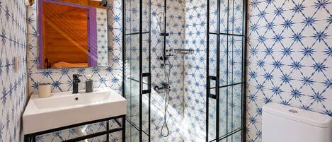 A bathroom with a shower, sink, and toilet, featuring blue star-patterned tiles and wooden ceiling.