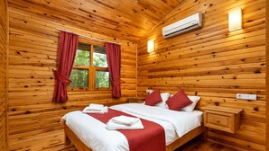 Een houten kamer met een bed, een nachtkastje, een airconditioningapparaat en een raam met gordijnen.