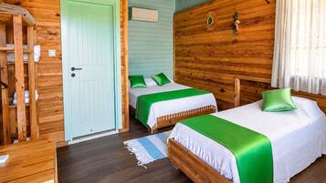 Una habitación con dos camas, un armario de madera, una puerta y una ventana pequeña con cortinas.