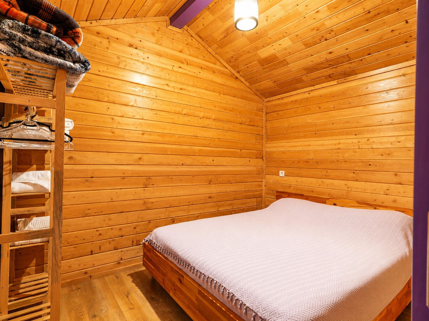 Une chambre dans un chalet en bois, avec un lit, une étagère avec des serviettes et un porte-manteau mural.