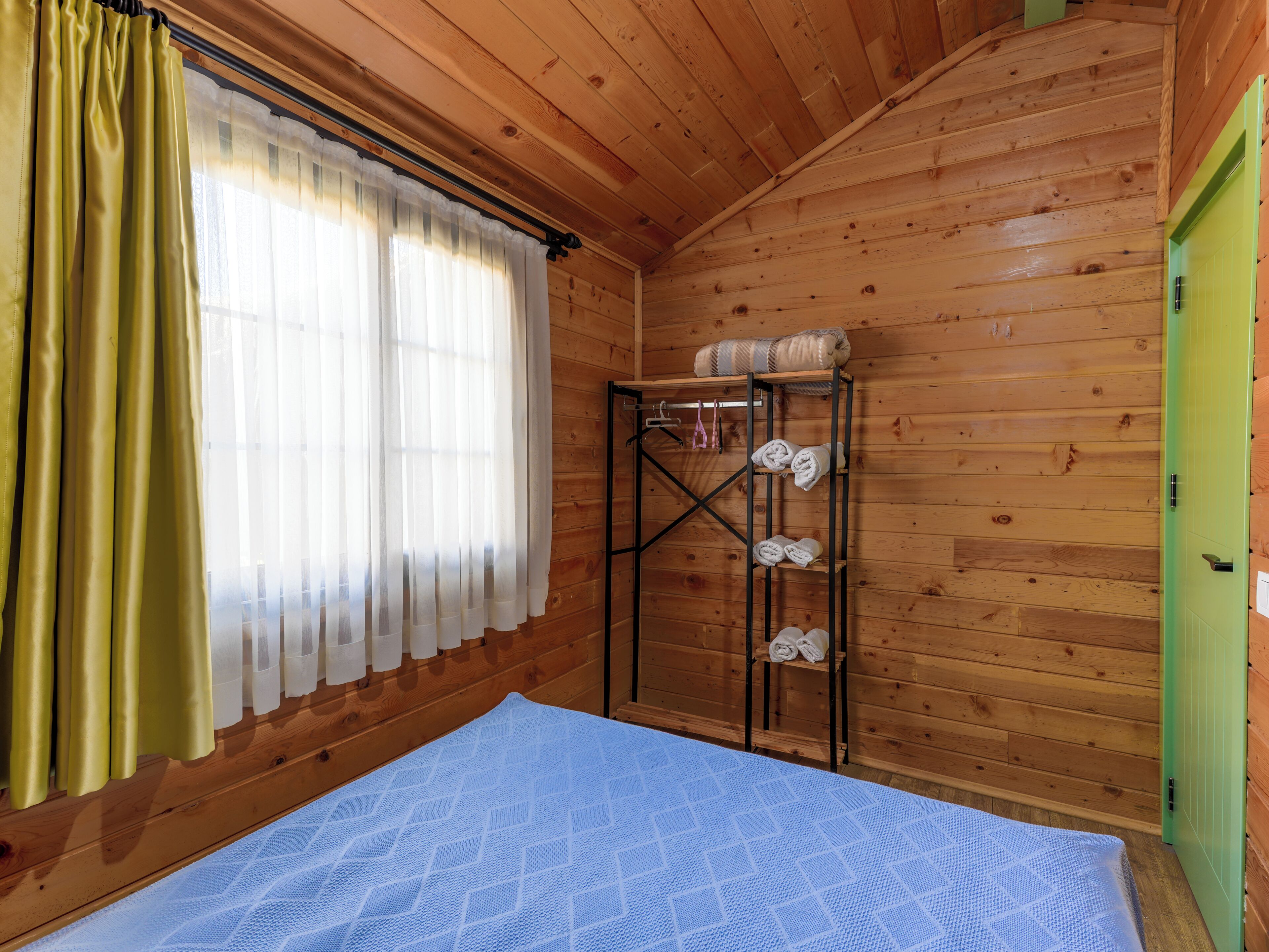 Una habitación de cabaña de madera con una cama, un estante con toallas y una puerta verde.