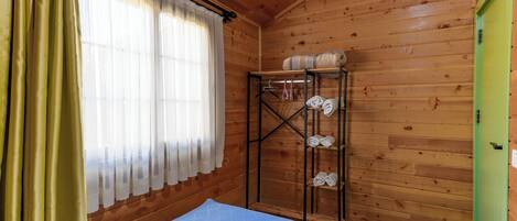 Una habitación de cabaña de madera con una cama, un estante con toallas y una puerta verde.
