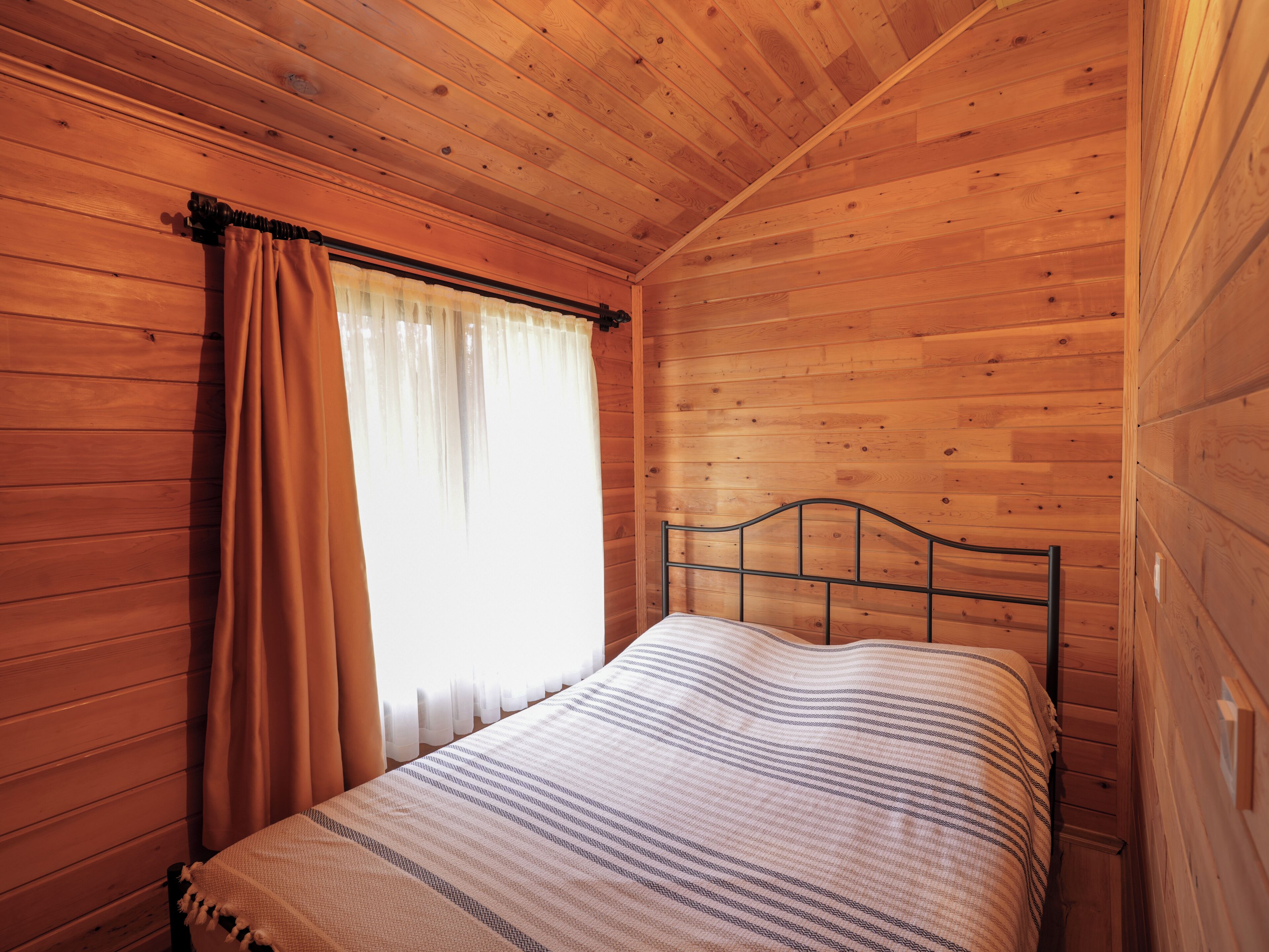 A wooden-paneled room with a bed, curtains, and a window.