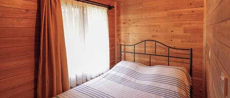 A wooden-paneled room with a bed, curtains, and a window.