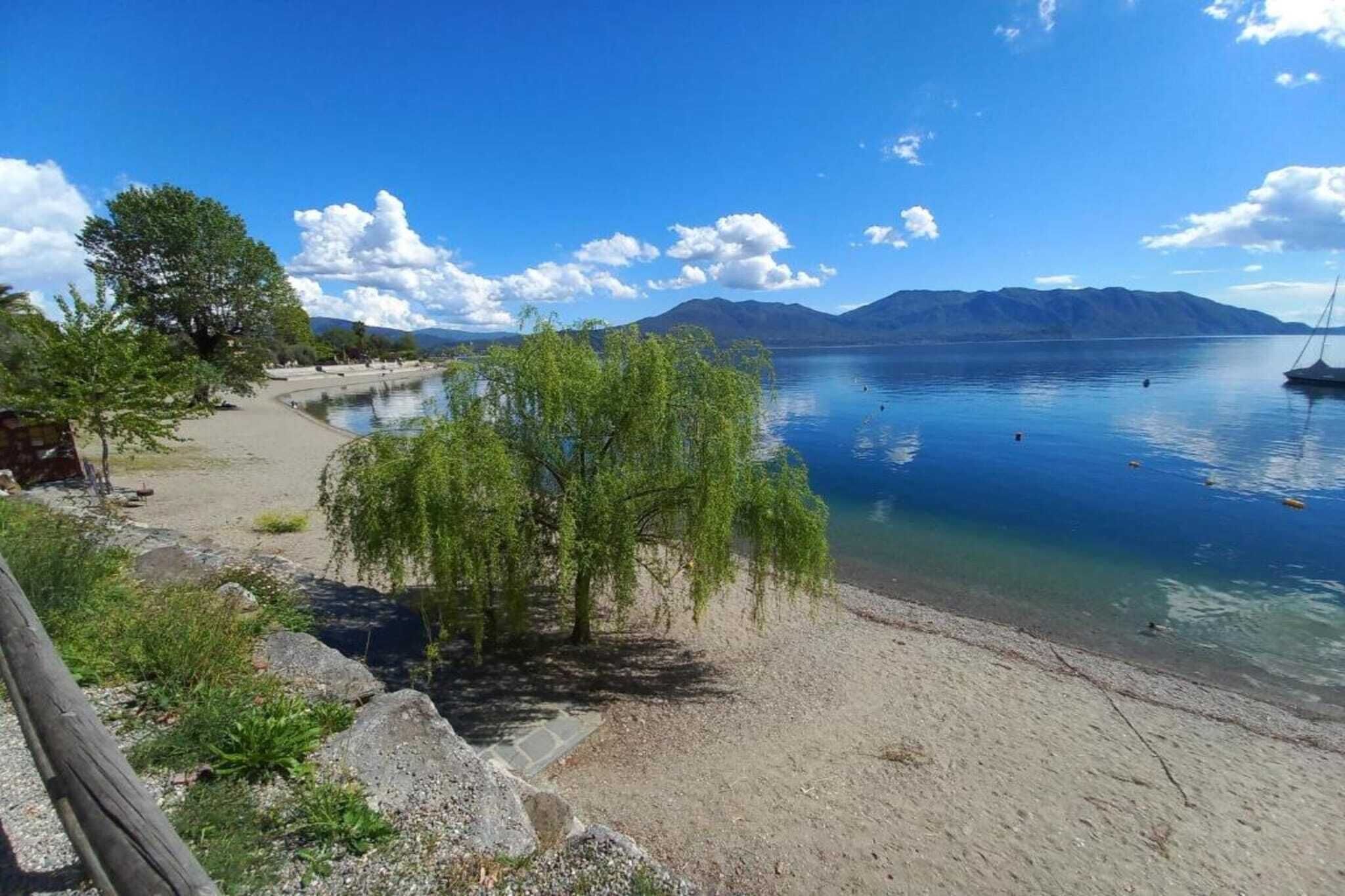 Näkymä järvelle, jossa on hiekkaranta, puita ja taustalla vuoria.