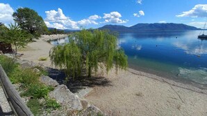 Vista a la orilla de un lago con una playa arenosa, árboles y montañas al fondo.