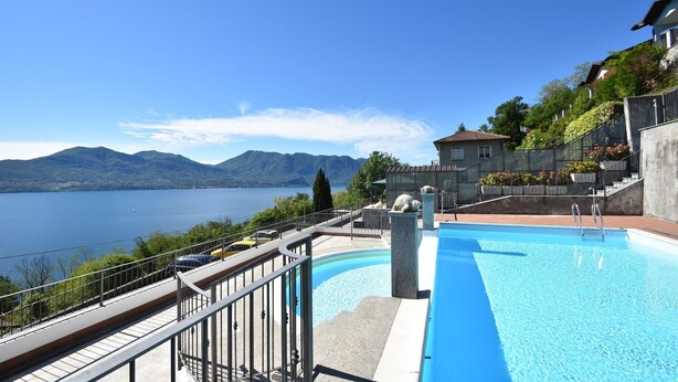 Una piscina con vistas a un lago y montañas, un muro de piedra y un edificio con techo inclinado.