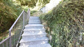 Una escalera de piedra con barandillas de metal que sube por una colina, rodeada de abundante vegetación.