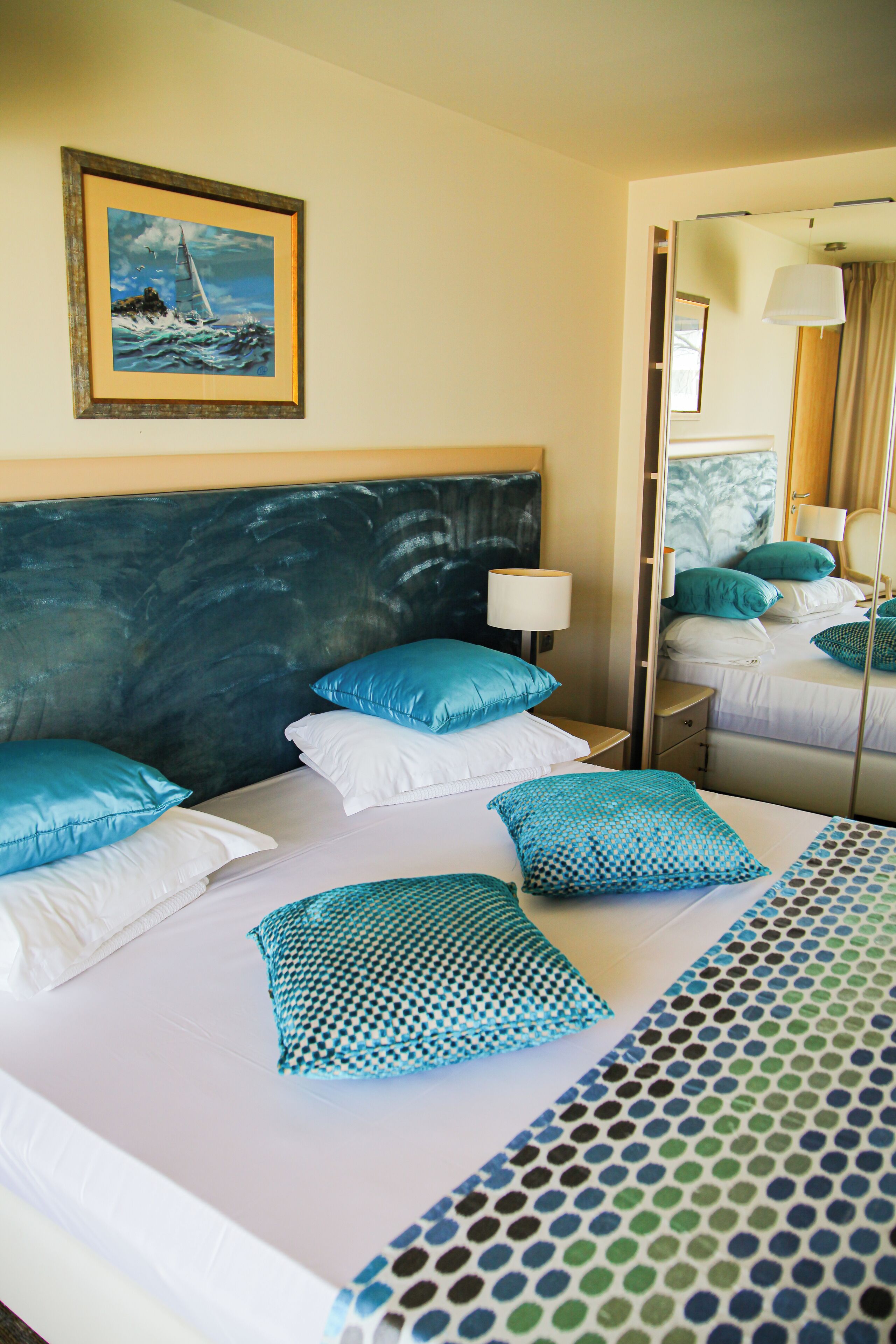 Una habitación de hotel con una cama grande, dos mesitas de noche, un espejo y un cuadro de un velero en la pared.