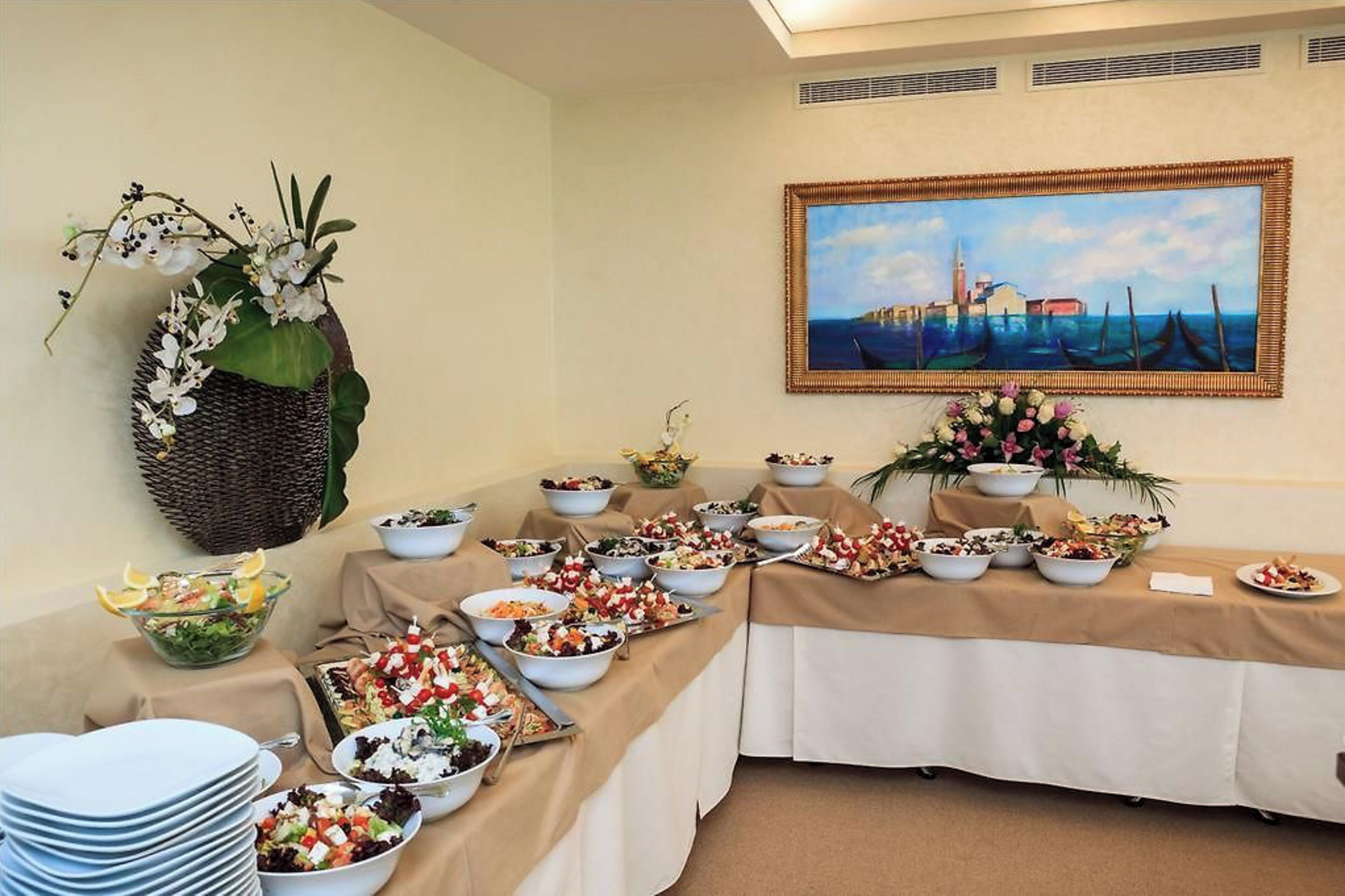 Uma mesa de buffet com diversos pratos e uma pintura de uma paisagem costeira.