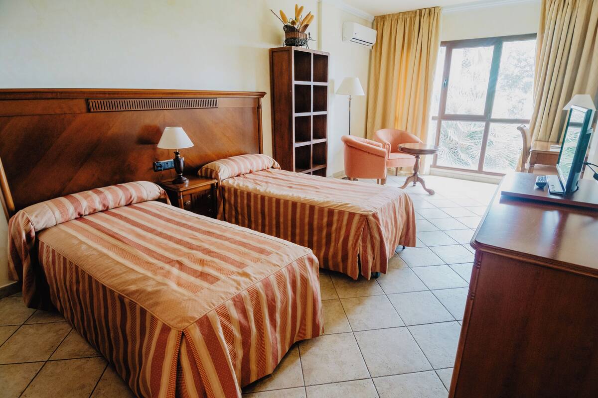 A hotel room with two beds, a desk, a chair, a wardrobe, and a window with curtains.