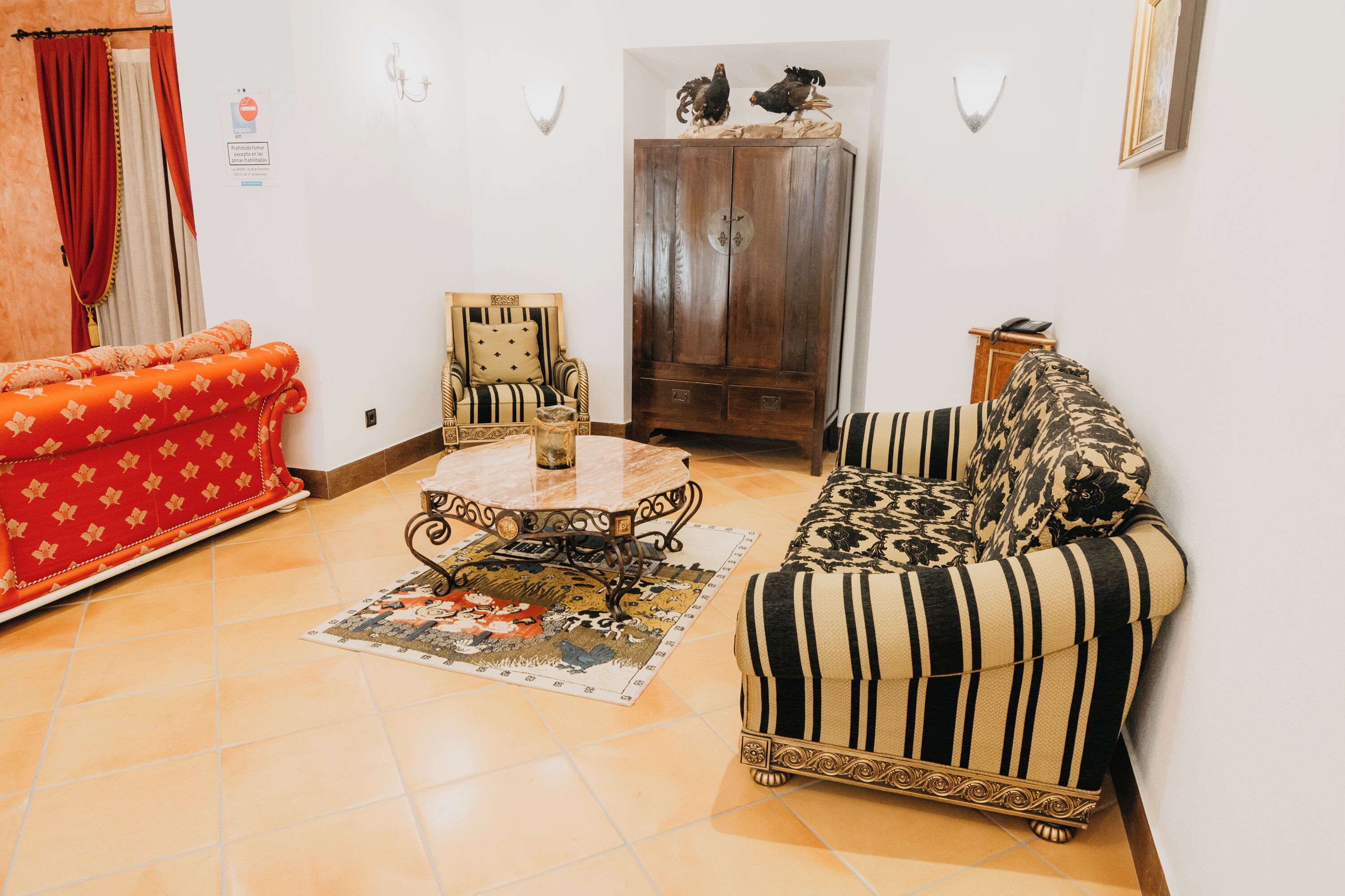 A living room with a red sofa, a striped sofa, a wooden cabinet, and a patterned rug.