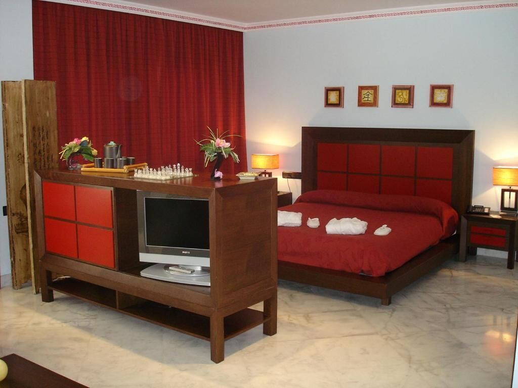 Een hotelkamer met een houten tv-meubel, een bed met rode beddengoed en een rood gordijn.