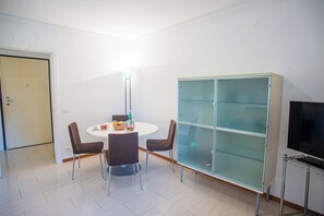 A dining area with a round table, four chairs, a cabinet with glass doors, and a television on a stand. - Matteo's Flat (Sanremo)
