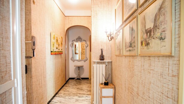Un couloir aux murs ornés de motifs, doté d’un sol en marbre, d’un miroir, d’une petite table et de tableaux encadrés.
