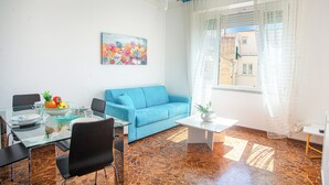 Un salon avec un canapé bleu, une table à manger avec des chaises, une table basse et un tableau accroché au mur.