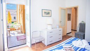 Une chambre d’hôtel comprenant un lit, un bureau, une chaise, une commode et une porte donnant sur un balcon.