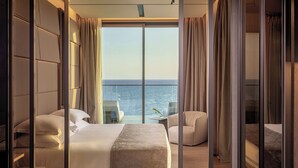 A hotel room with a large bed, a seating area, and a view of the sea. - Amathus Residences (Limassol)