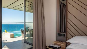 A modern hotel room with a large sliding glass door leading to a balcony with a pool and ocean view.