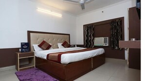 Une chambre avec un grand lit, une table de chevet, un ventilateur de plafond, un climatiseur mural et un tapis violet.