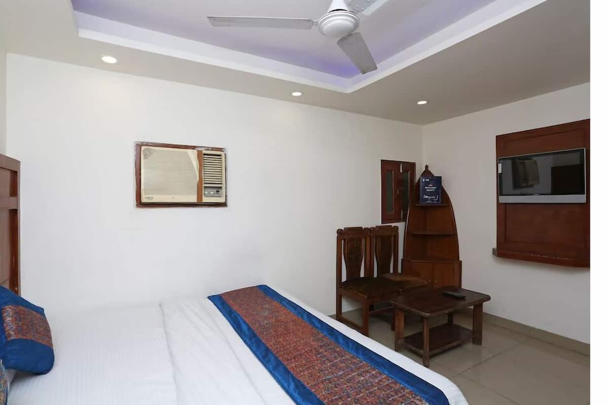 Una habitación de hotel con una cama, un ventilador de techo, una silla de madera, una mesita pequeña y un televisor montado en la pared.