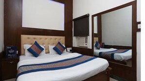 Une chambre d’hôtel avec un grand lit, une tête de lit, une table de chevet, une commode, un miroir et un téléviseur fixé au mur.