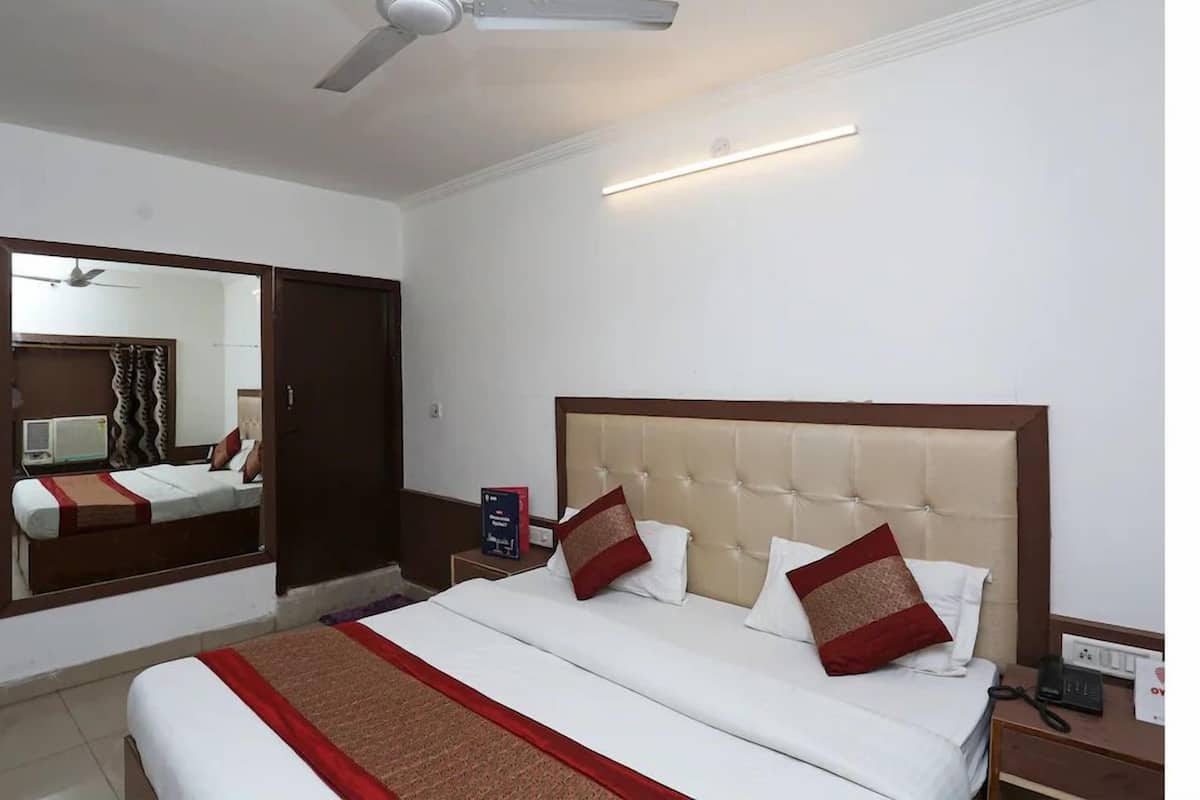 Una habitación de hotel con una cama grande, un ventilador de techo, una mesita de noche con teléfono y un espejo en la pared.
