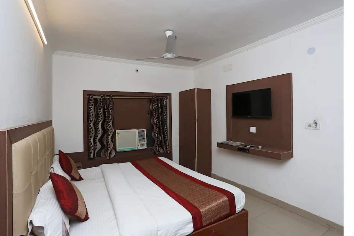 Una habitación de hotel con cama, ventilador de techo, aire acondicionado, televisor montado en la pared y una pequeña estantería.