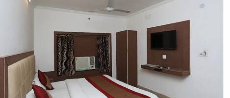 Une chambre d’hôtel équipée d’un lit, d’un ventilateur de plafond, d’un climatiseur, d’un téléviseur fixé au mur et d’une petite étagère.