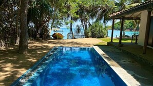 A rectangular pool with clear blue water, surrounded by trees and a view of the sea.