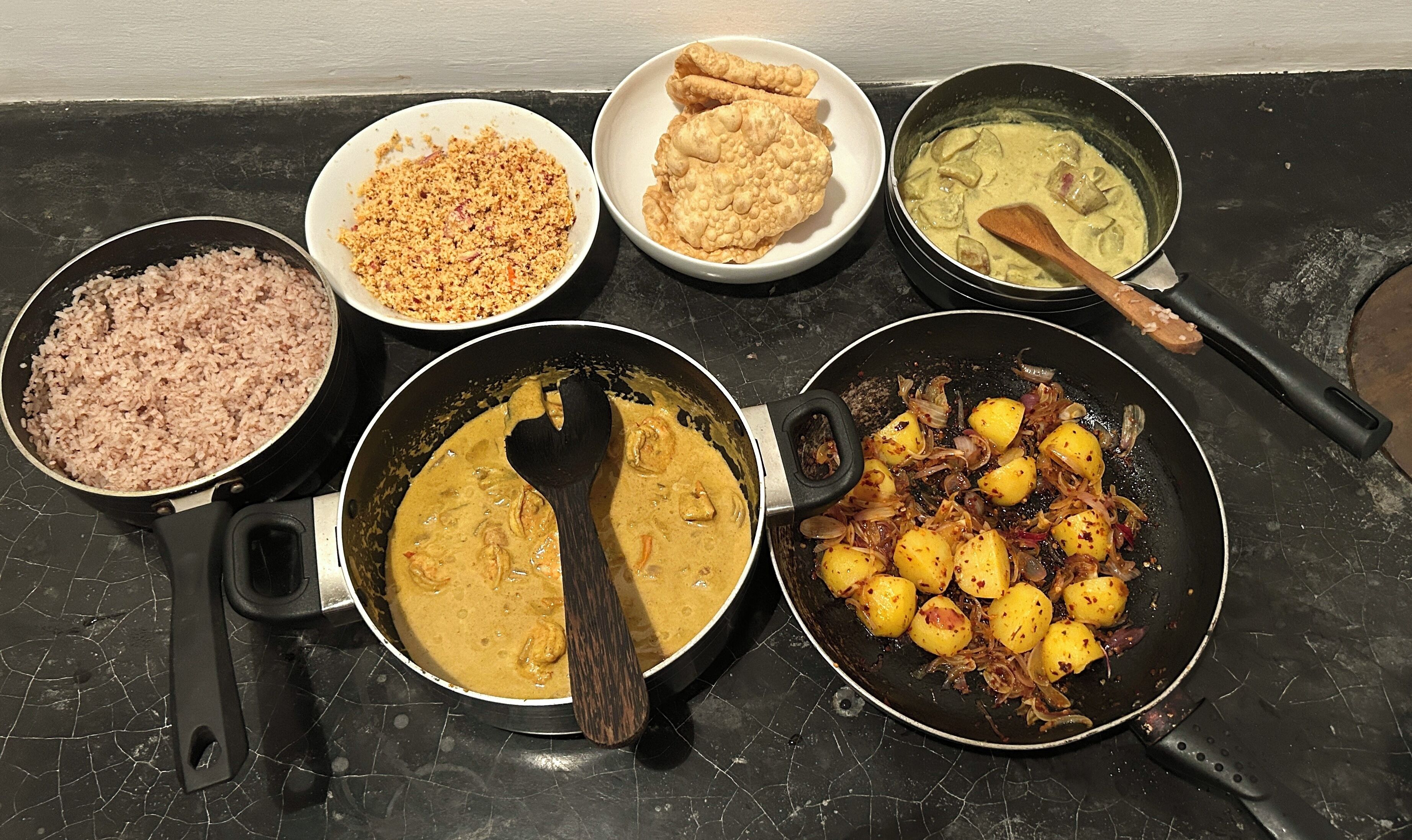 A kitchen counter with various dishes including rice, a curry, and fried items.
