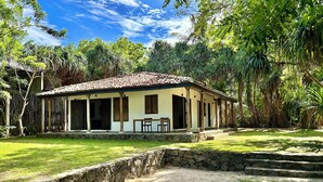 A house with a tiled roof, a porch with chairs, and a stone wall in front.