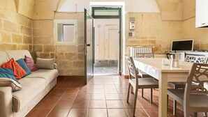 A cozy room with a stone wall, a beige sofa with colorful cushions, a wooden dining table, and a tiled floor. - 3936 Corte dei Falconi by Barbarhouse (Lecce)