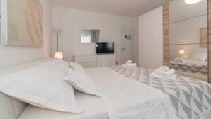A hotel room with two beds, a TV, a mirror, and a painting on the wall.