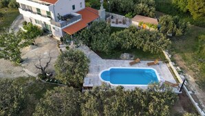 A modern two-story house with a swimming pool, surrounded by dense greenery.