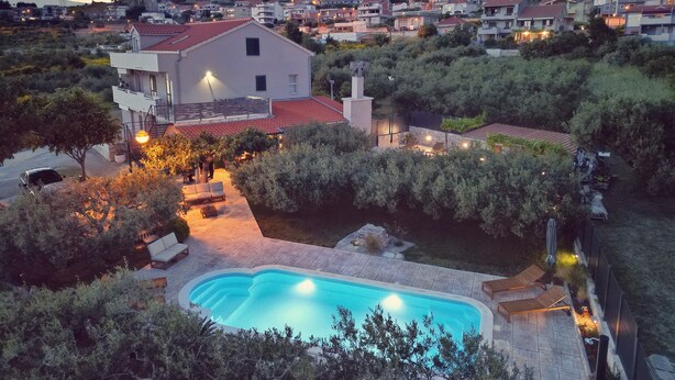 A residential area with a swimming pool, a large house with a red roof, and a hillside in the background.