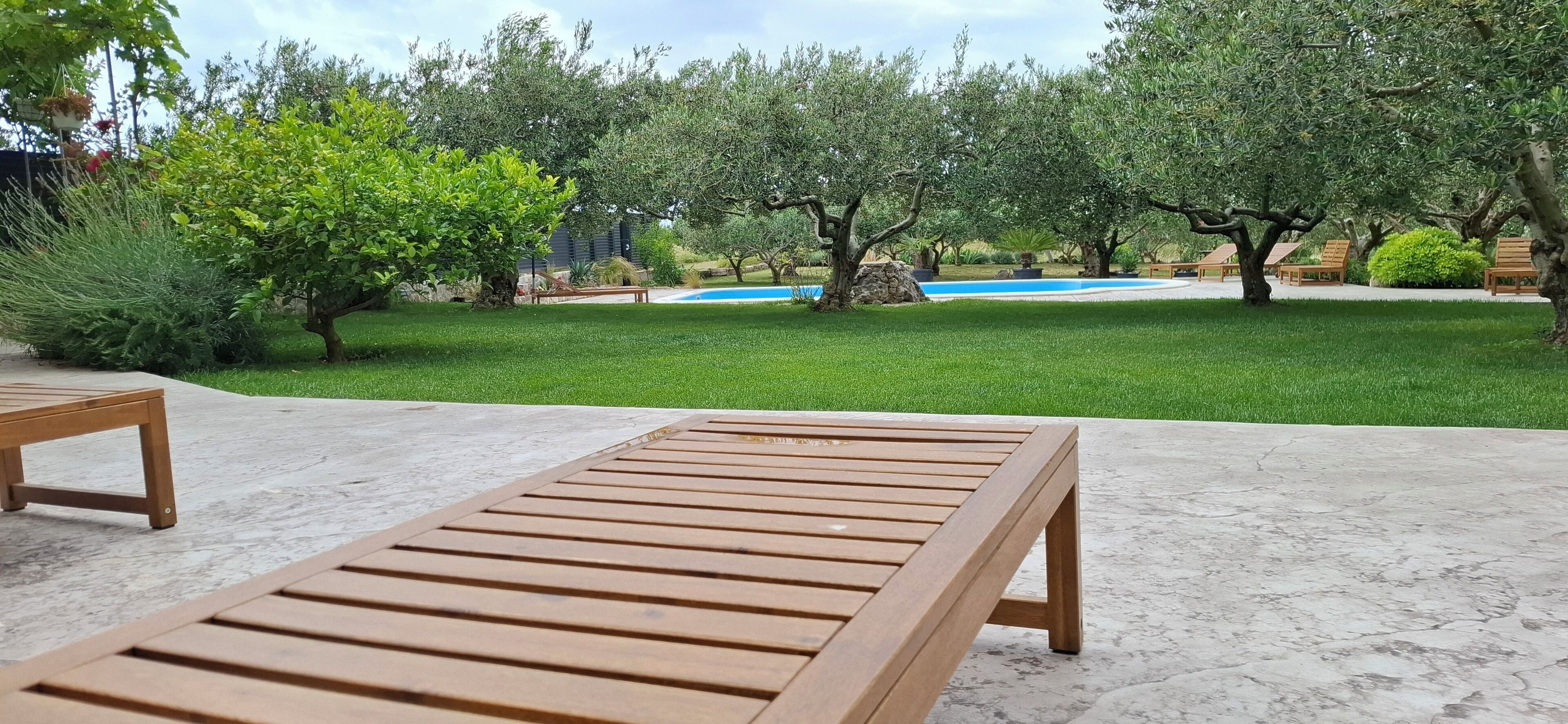 Una terraza de madera con piscina y exuberante follaje al fondo.