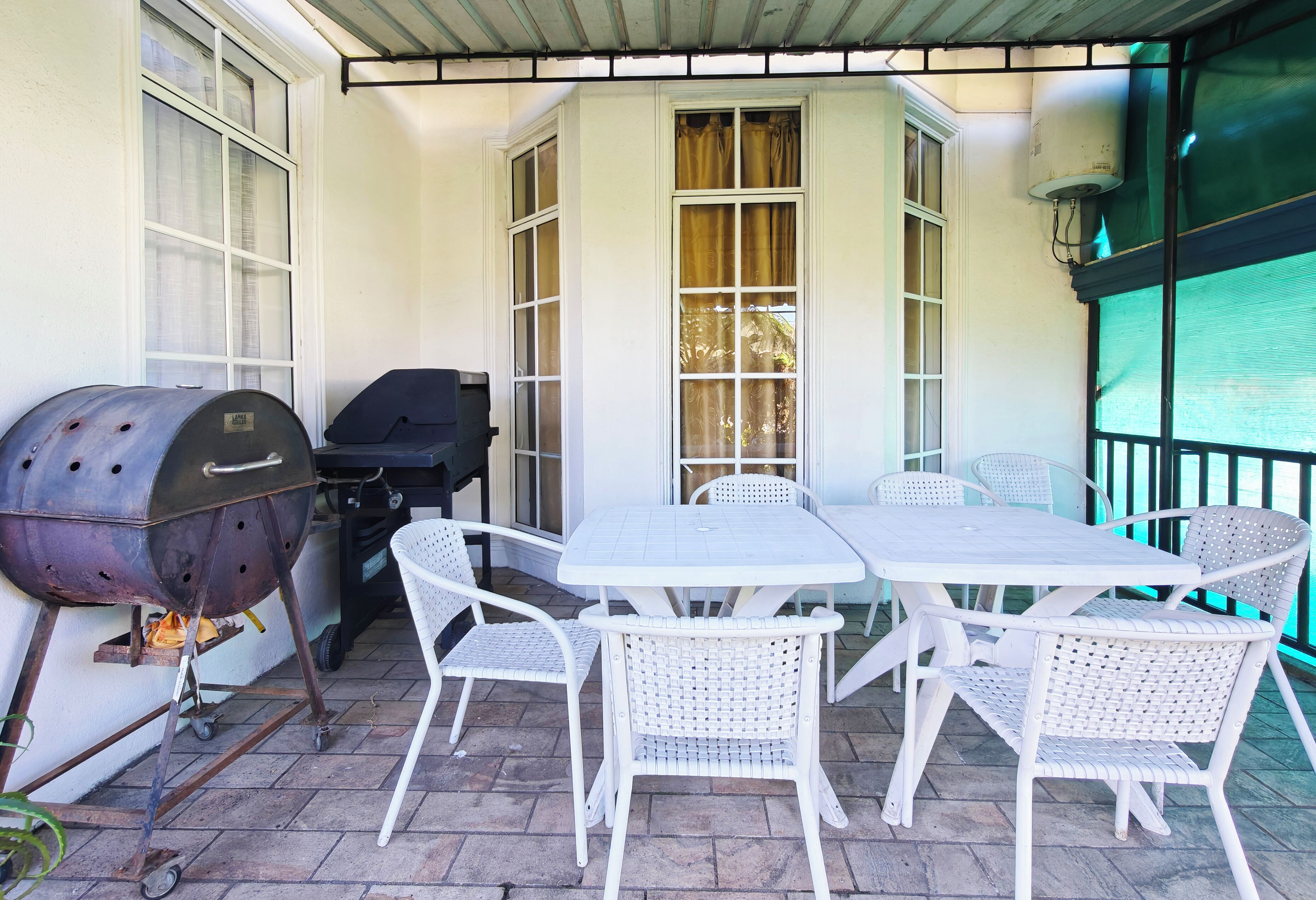A patio with a grill, white wicker chairs, and a table.