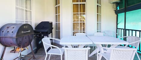 A patio with a grill, white wicker chairs, and a table.