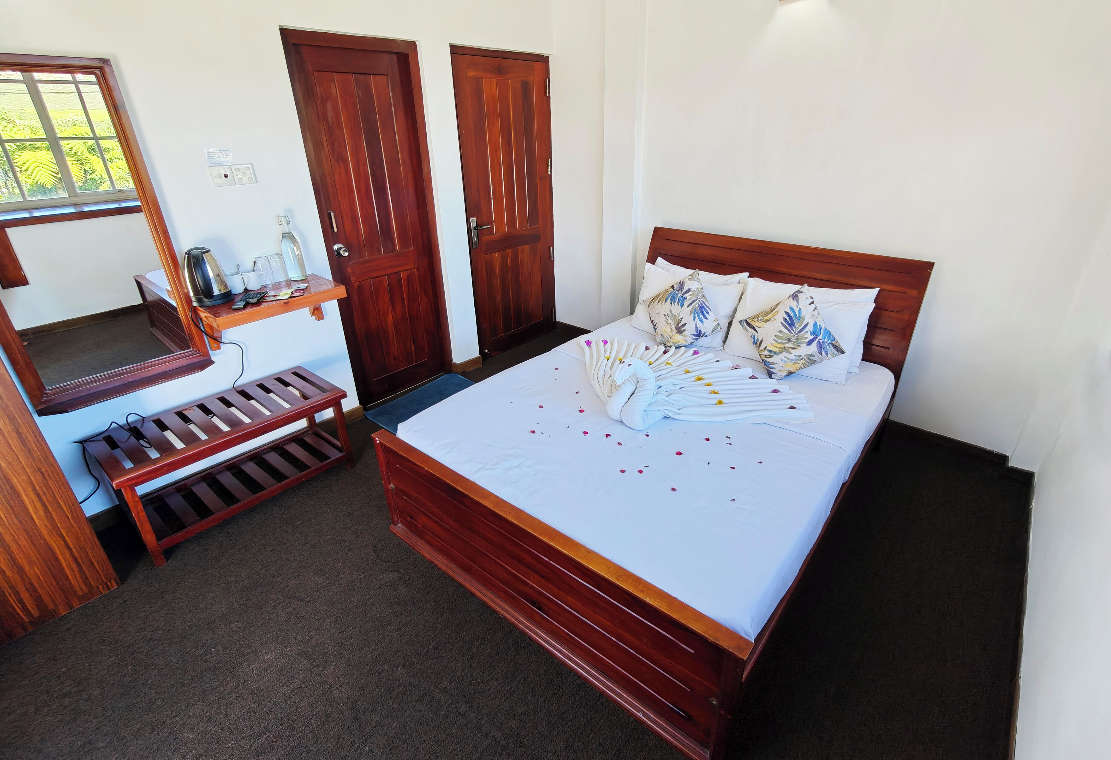A bedroom with a wooden bed, a bench, a mirror, and a shelf with a kettle and glasses.