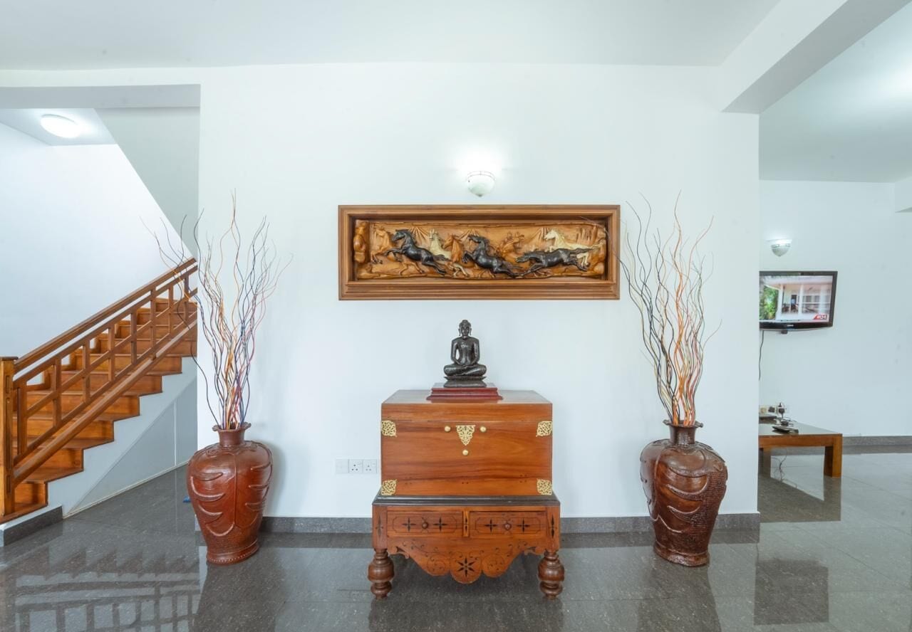 Un área de recepción con una escalera de madera, un mueble de madera con una estatua de Buda y dos jarrones decorativos.