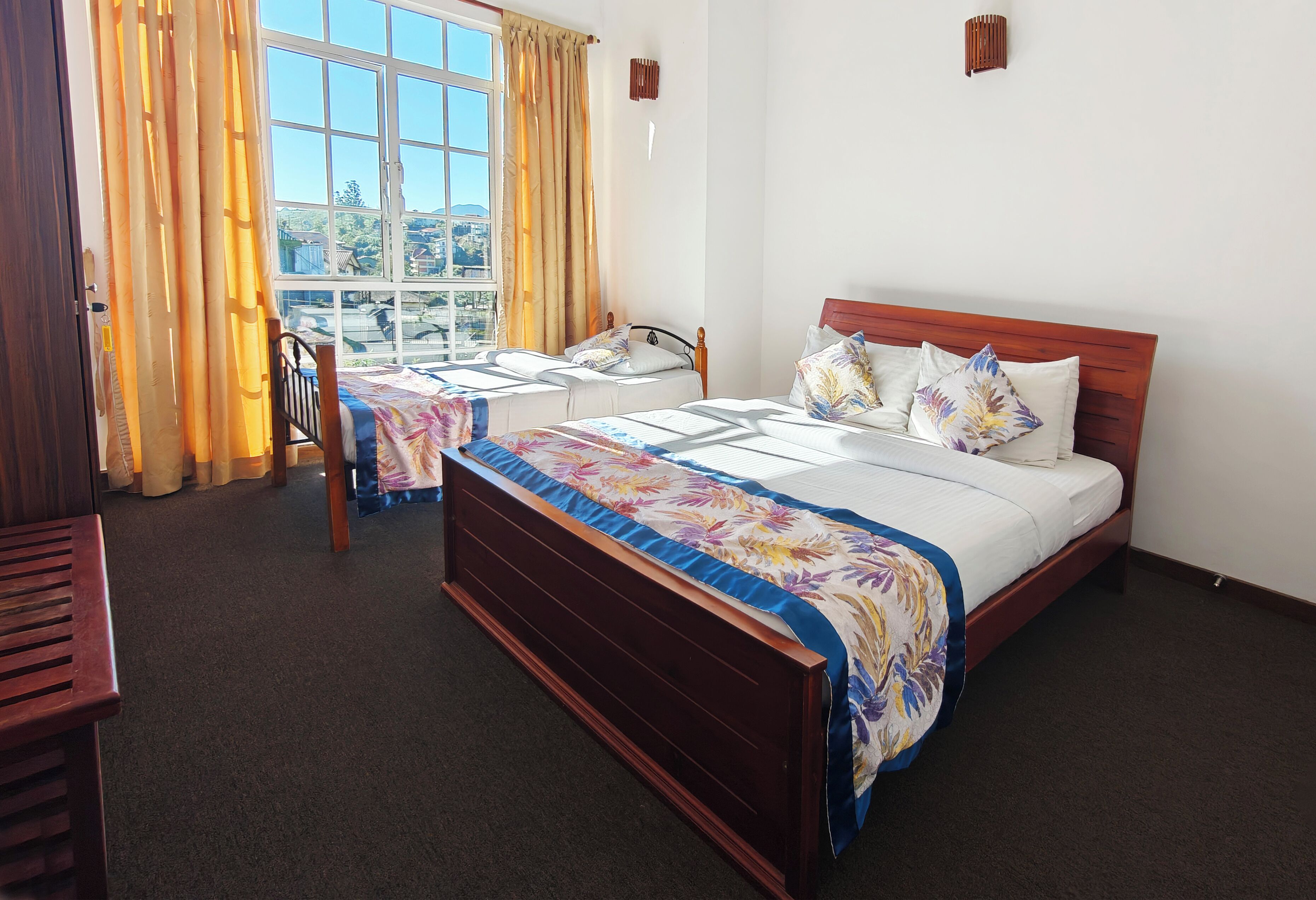 A hotel room with two single beds, a wooden headboard, a window with curtains, and a view of the outside.