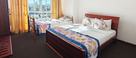 A hotel room with two single beds, a wooden headboard, a window with curtains, and a view of the outside.